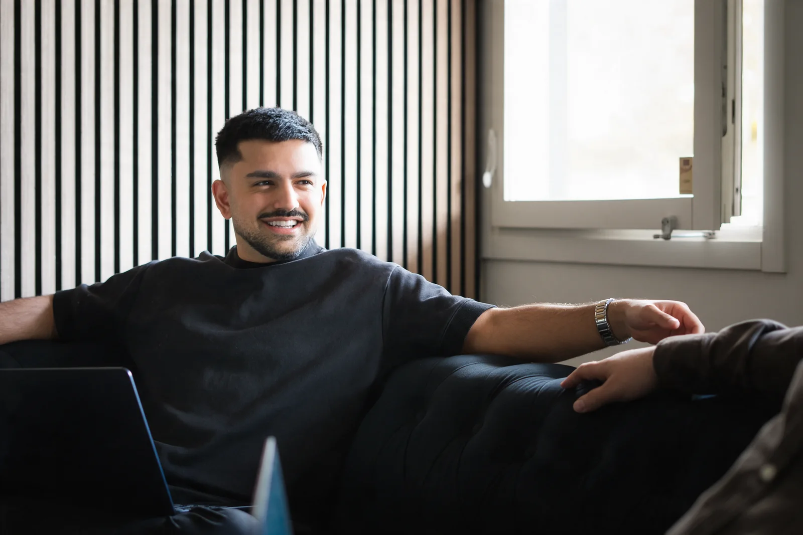 Shayan Parsai smiling on a sofa with his laptop
